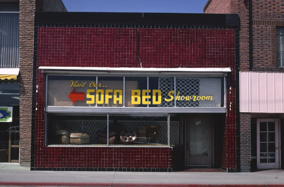 A red-tiled furniture store front with a neon “Sofa Bed Showroom” sign